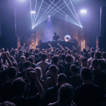 A DJ in a cirowded room with crowd listening intently to music selections while dancing